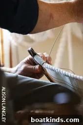 Sailmaker using a leather palm and waxed thread to hand-stitch a sail